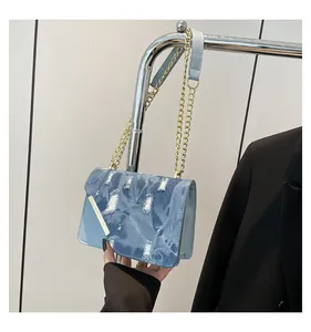 Detail of light blue denim flap bag with gold chain strap and distressed texture
