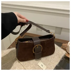 Détail du sac sous le bras en daim marron avec boucle dorée et finitions en cuir