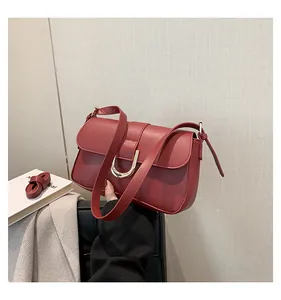 Detail of burgundy matte leather shoulder bag with gold horseshoe clasp and strap