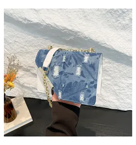 Detailed shot of denim patchwork flap with frayed edges and golden chain strap on a bag