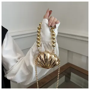 Detail of a gold shell-shaped evening clutch bag with glossy metallic texture and bead chains