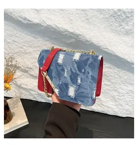 Detail of blue denim and red leather crossbody bag with gold chain strap and metal frame