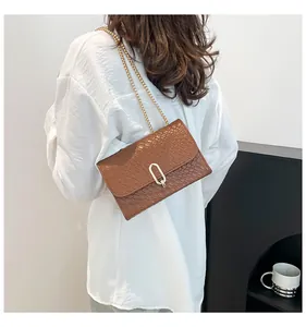 Détail d'un sac marron à motif tressé avec boucle dorée en U et bandoulière en chaîne métallique