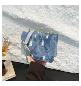 Detail of blue denim and leather crossbody bag with gold chain strap on rock wall
