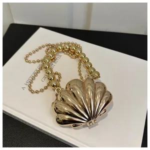 Detail of a luxury gold shell clutch bag with a pearl bead handle and chain strap