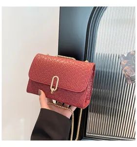 Détail du sac rouge brique à motif crocodile avec boucle dorée tenu par un mannequin