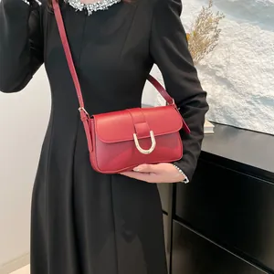 Elegant dark red leather crossbody bag with gold U-shaped hardware on a black dress