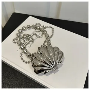 Detail shot of a silver shell-shaped handbag with metallic texture and beaded chain strap