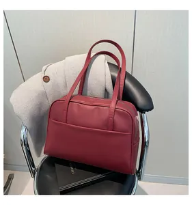 Gros plan du sac cabas en similicuir bordeaux avec poche frontale sur une chaise noire