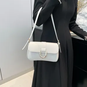 Elegant white minimalist leather shoulder bag with a gold U-shaped buckle on a black dress