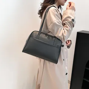 Grand sac cabas minimaliste noir en similicuir porté à l'épaule avec un trench beige
