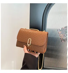 Détail de la texture en cuir crocodile marron avec boucle ovale dorée et bandoulière chaîne