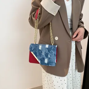 Fashionable denim chain shoulder bag with red contrast panels and gold V-shaped metal trim