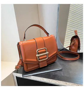 Detail showing caramel brown handbag with golden buckle and crossbody strap in a mirror reflection