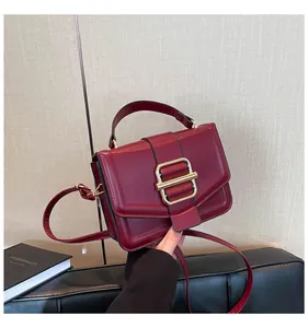 Close-up of burgundy leather crossbody bag with a large gold square metal buckle detail