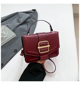 Close-up of wine red leather handbag featuring a golden square buckle and rounded handle