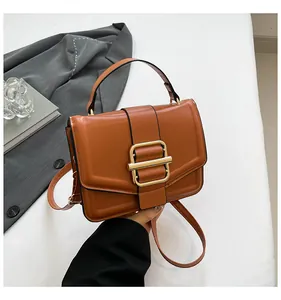 Close-up of caramel leather handbag featuring a prominent gold square buckle and handle