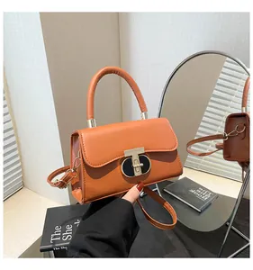 Detail view of the orange crossbody bag with a metallic T-clasp and leather handle