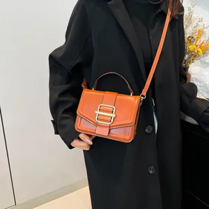 Caramel leather square handbag with gold lock shown with a black coat by a model