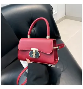 Close-up of vibrant red leather handbag with golden metal T-lock on a black sofa