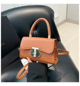 Detailed view of brown leather bag with a distinctive golden T-shaped metal lock closure