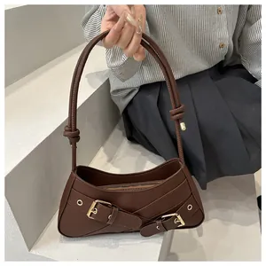 Detail of brown baguette bag with leather cross straps and gold buckle accents