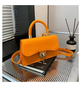 Detail of bright orange leather handbag with silver metallic twist lock and top handle