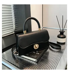 Detail of black handbag showing wavy flap design and golden circular twist lock closure