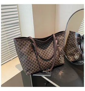 Detail der braunen Shopper-Tasche mit M-Muster und goldenem Anhänger-Anhänger