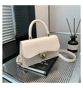 Detailed view of cream-colored small square bag with wavy flap and gold metal twist lock