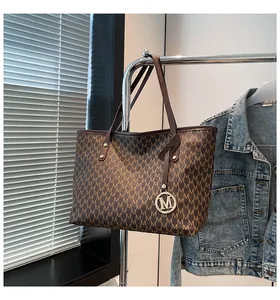 Detailansicht der braunen Monogramm-Tragetasche mit goldenem M-Metallanhänger-Detail