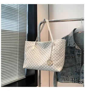 Detaillierte Nahaufnahme einer weißen Tote Bag aus Leder mit grauen M-Mustern und Goldanhänger