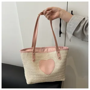 Détail d'un sac cabas tissé avec un écusson cœur en cuir rose et anses assorties