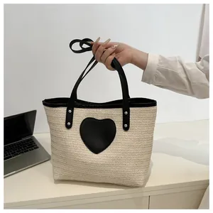 Détail du sac cabas en paille tissée avec écusson cœur noir et ordinateur sur table