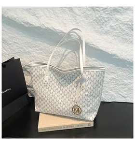 Detailansicht der grauen Monogramm-Tasche mit goldenem M-Anhänger auf Designbuch