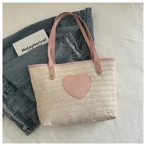 Détail du sac cabas tissé avec écusson cœur rose et rivets renforcés sur les poignées