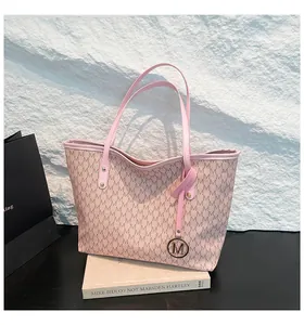 Nahaufnahme der rosa Tragetasche mit M-Monogramm und rundem Metallanhänger auf Buch