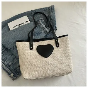 Détail du sac cabas tissé avec un écusson cœur en cuir noir et des rivets en métal