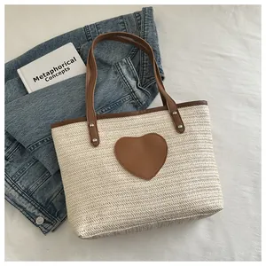 Détail du sac cabas en paille tressée avec un patch cœur marron et des anses en cuir