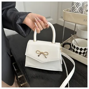 Detail of white square handbag showing golden bow buckle and fine leather texture