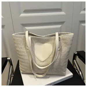 Détail d'un sac cabas tissé crème avec un patch cœur en cuir et des fines bandoulières