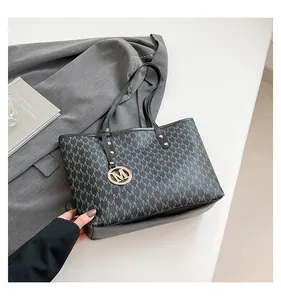 Detailed top view of a black monogram tote bag with gold M-shaped charm and slim handles