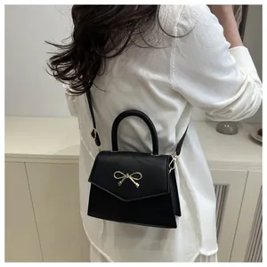 Detail of a black mini crossbody bag with a gold bow buckle on a model's back