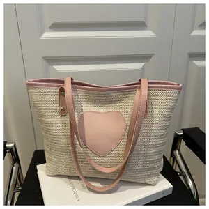 Détail d'un sac cabas en paille tissée avec patch cœur rose et lanières en cuir synthétique