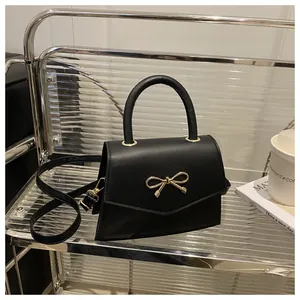 Close-up of black trapezoid handbag with elegant gold bow clasp and smooth leather finish