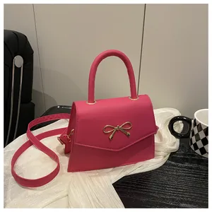 Detail of hot pink trapezoid handbag with gold bow ornament and adjustable shoulder strap
