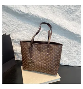 Detail of dark brown tote bag with M-letter monogram and gold metal charm pendant