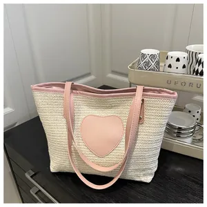 Détail d'un sac cabas en paille avec un patch en cœur et des anses en similicuir rose