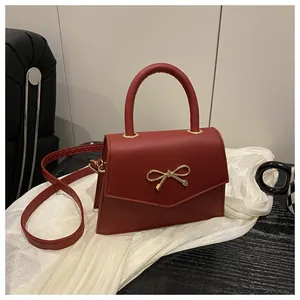 Detail of red crossbody bag with golden bow clasp on white silk background