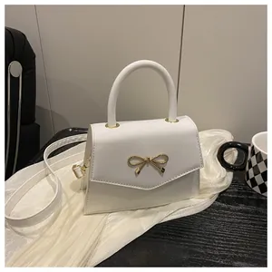 Detail of white square handbag with golden bow metal buckle on elegant silk fabric
